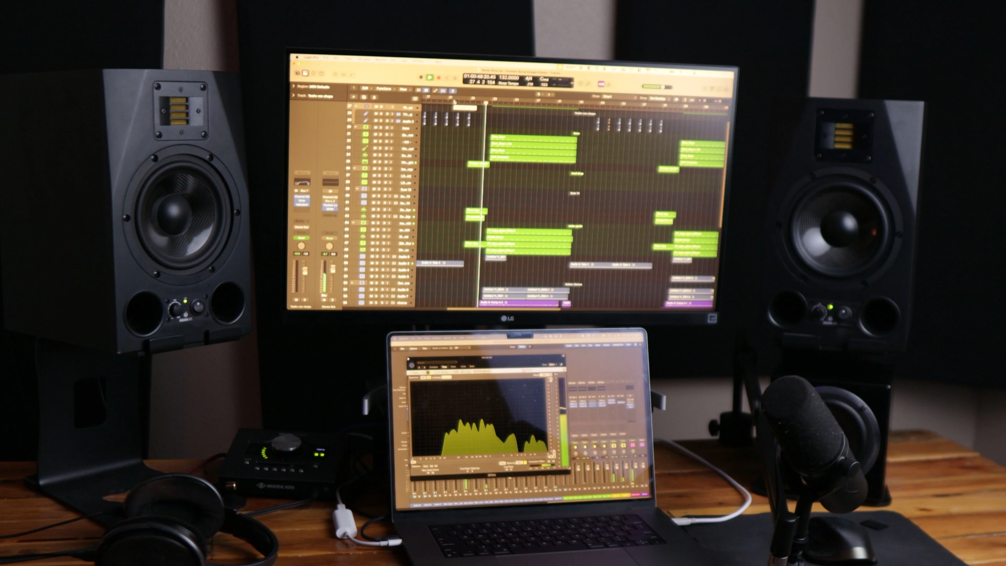 Professional home studio setup showing studio monitors, laptop running DAW software, and desktop monitor displaying audio tracks for music production