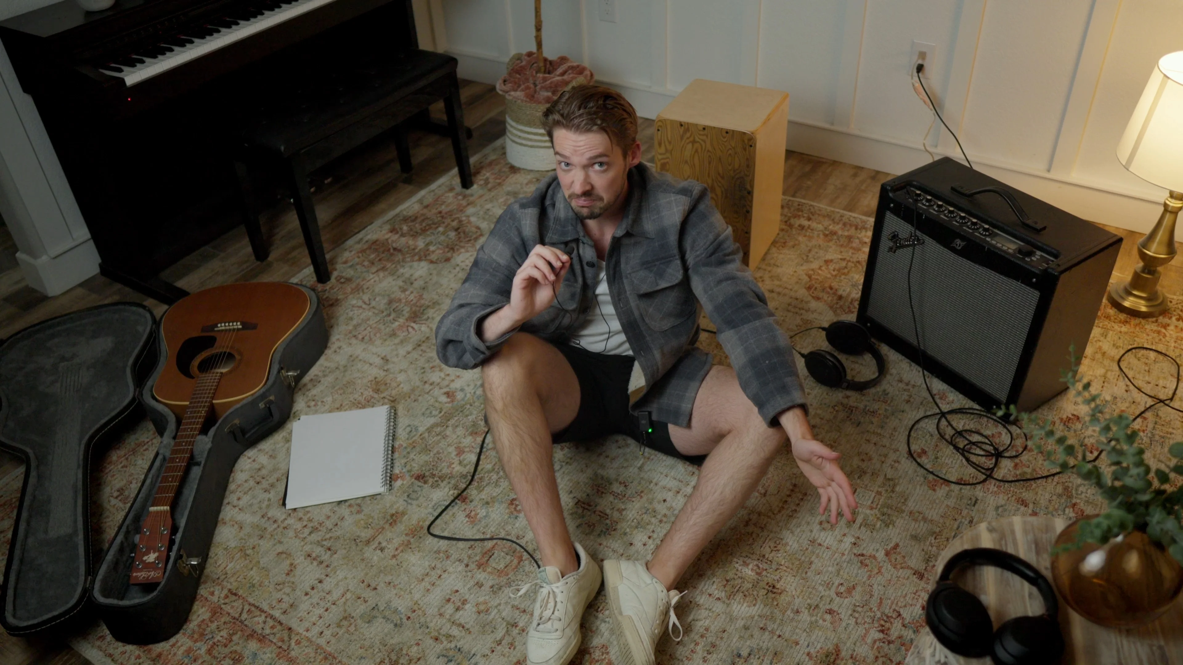 Mattie sitting on studio floor with acoustic guitar and notepad during a songwriting session, demonstrating the writing process for better vocals
