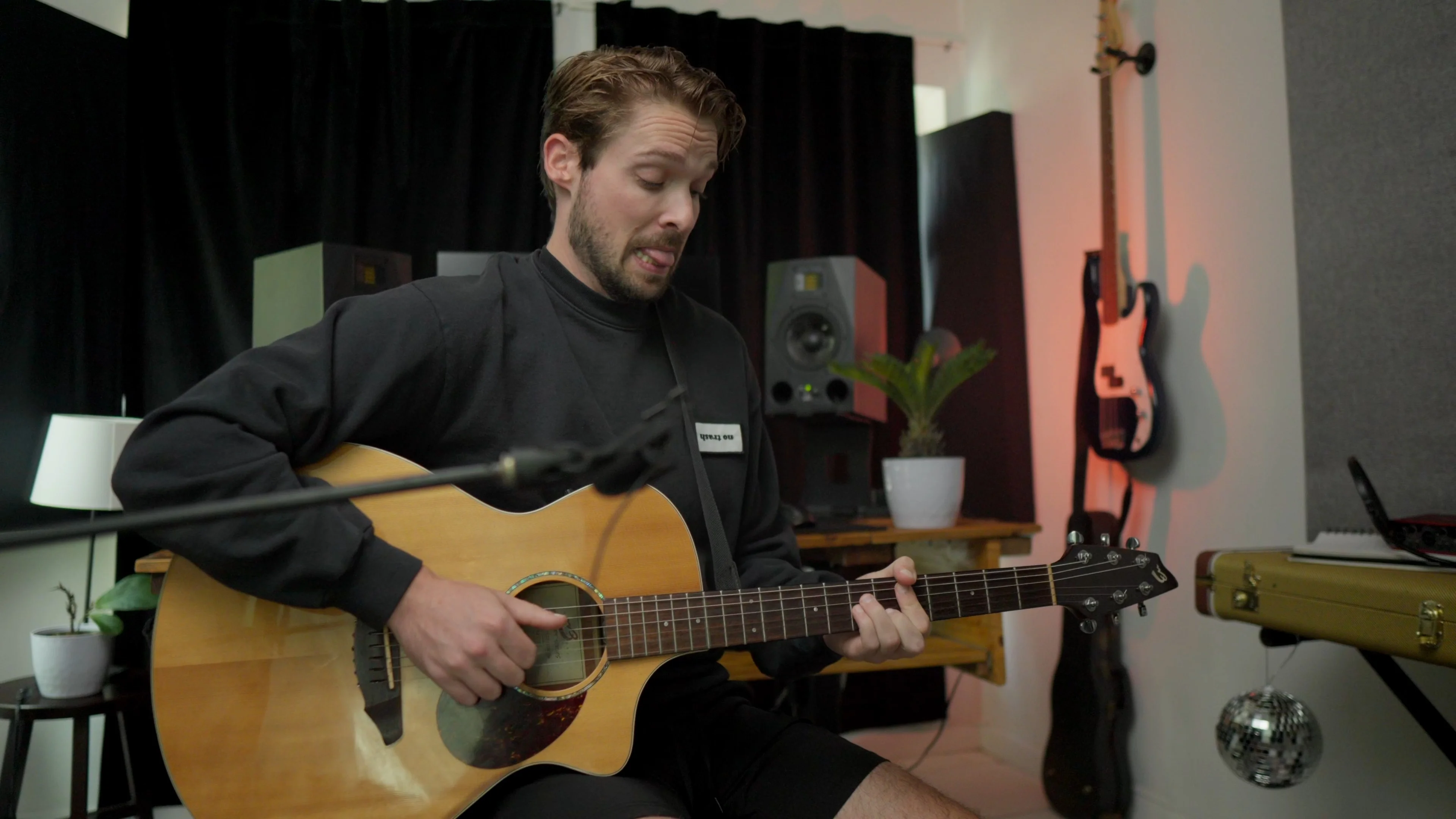 Mattie playing acoustic guitar in professional studio with monitors and recording equipment, demonstrating ambient guitar recording techniques