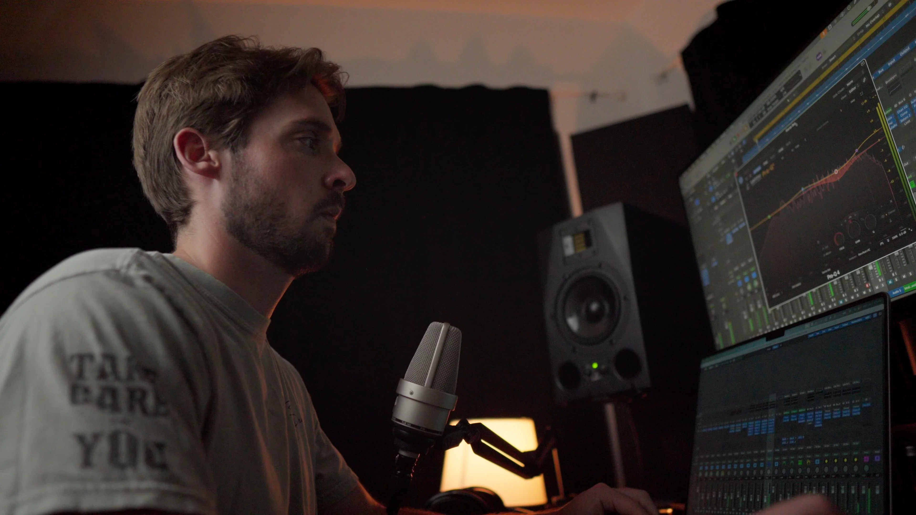 Mattie recording vocals with a condenser microphone in home studio while viewing Logic Pro session on dual monitors