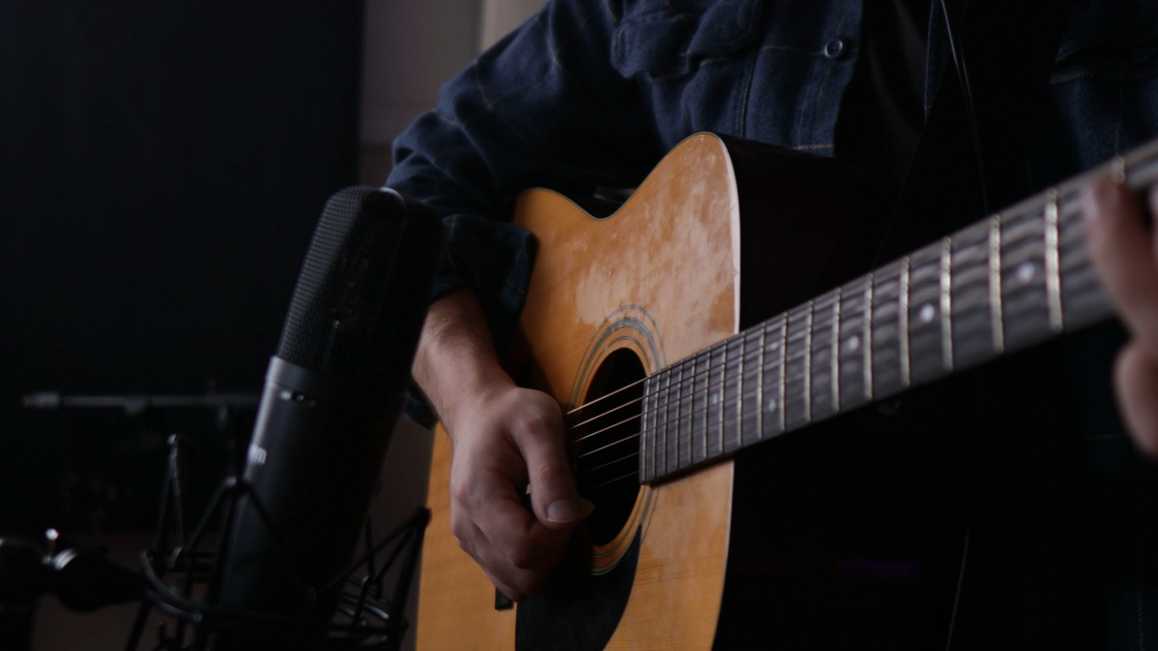 Mattie recording acoustic guitar with professional condenser microphone in treated home studio showing acoustic panels