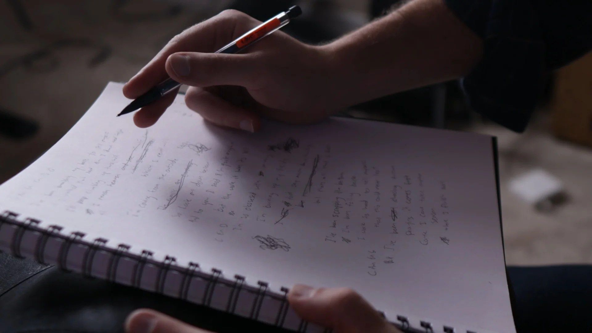 Mattie writing lyrics in a spiral notebook with a pen during a songwriting session, demonstrating the traditional method of lyric composition