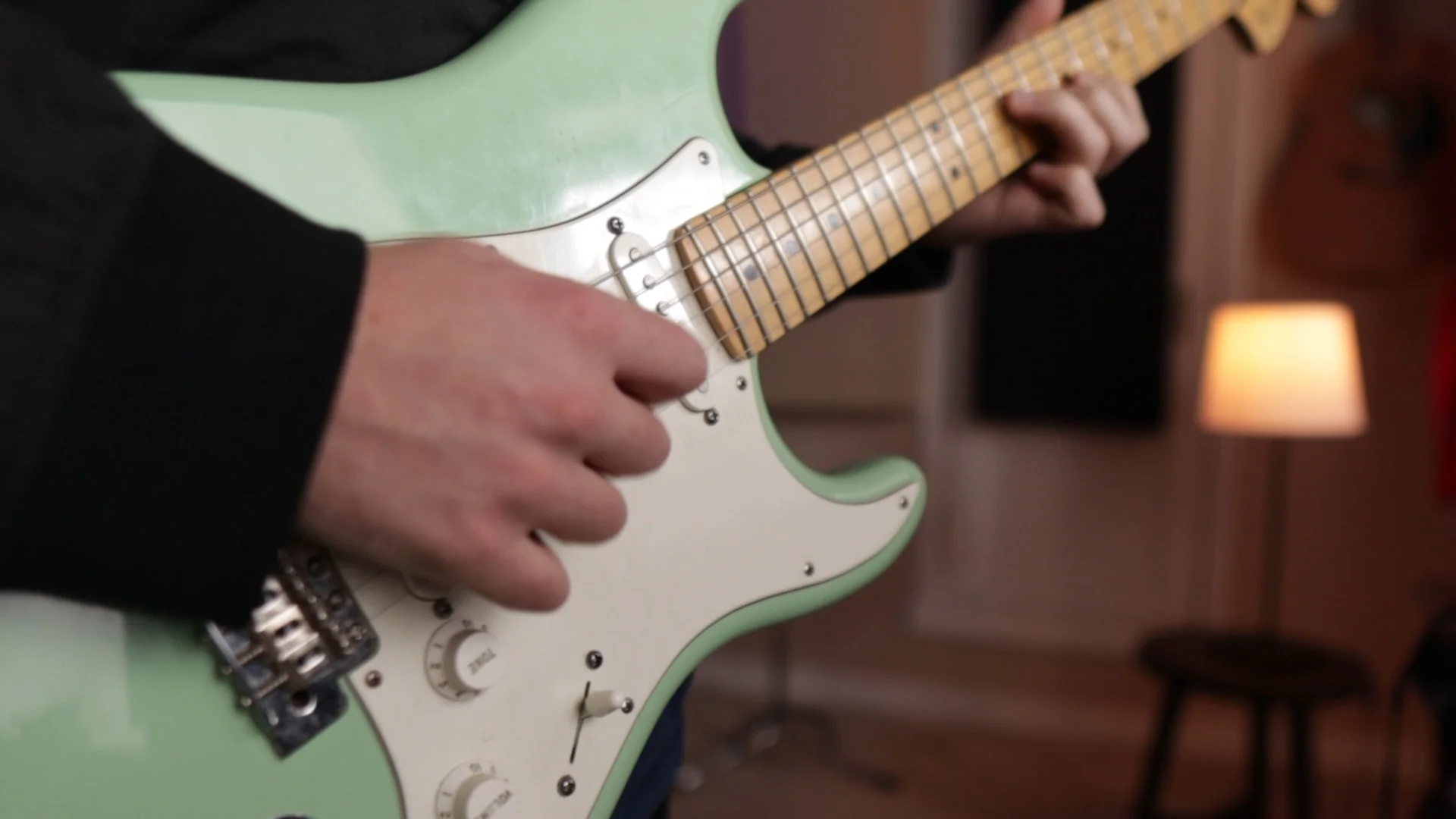 Close-up of mint green electric guitar being played, demonstrating the type of instrument processed through Logic Pro's amp and pedal plugins